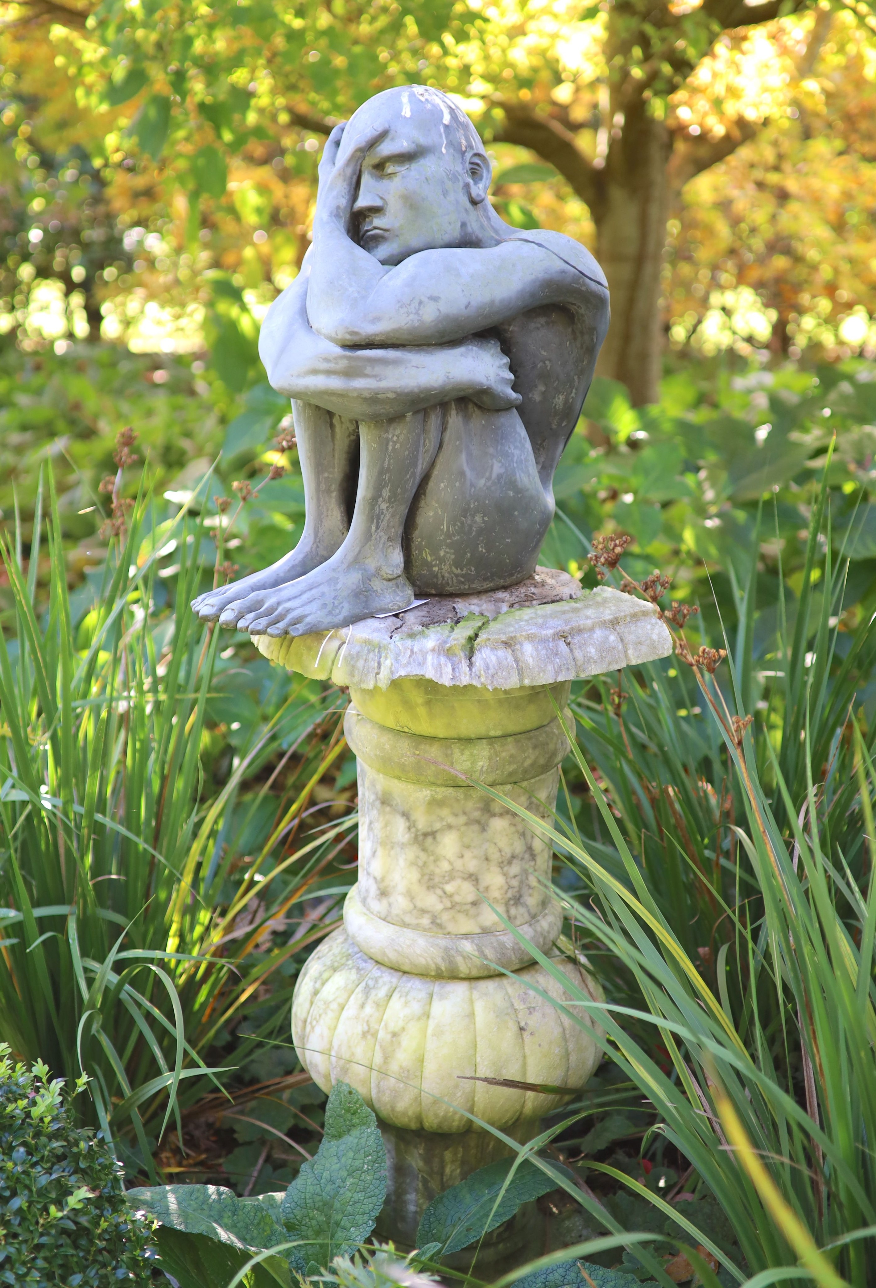 A simulated lead resin garden statue of a seated man, height 49cm, with a damaged marble pedestal, height 78cm